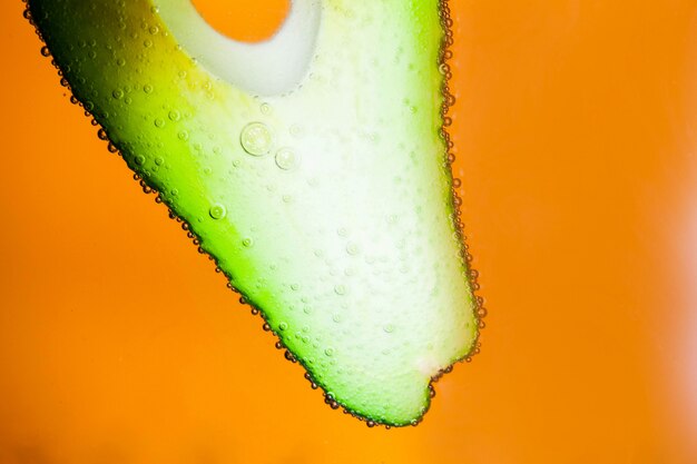 Air bubbles cover slice of avocado floating on orange background