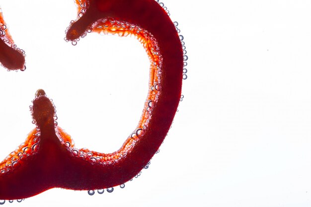 Air bubbles cover slice of red pepper in water on white background