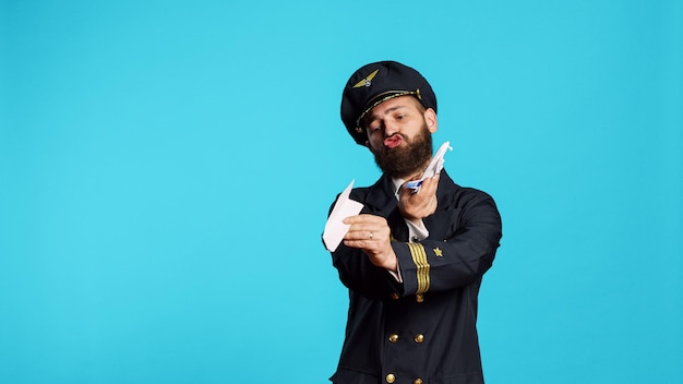 Бесплатное фото Пилот авиакомпании играет с бумагой и мини-самолетом, развлекается с оригами и маленьким искусственным самолетом в студии. молодой летчик-мужчина в летной форме, работающий на коммерческих рейсах.