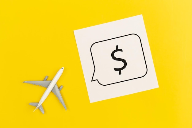 Airplane model and dollar sign on yellow background flat lay