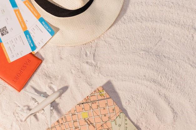 Free photo airplane and tickets with hat and map on sand