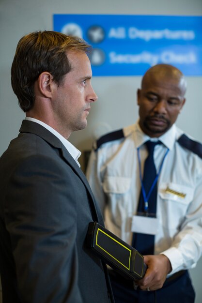 Сотрудник службы безопасности аэропорта использует ручной металлоискатель для проверки пассажира