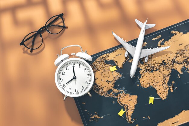 Alarm clock airplane miniature glasses and world map flat lay