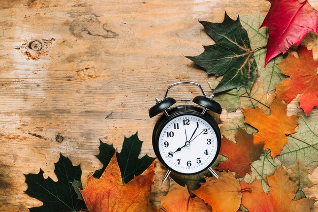 Alarm clock and autumn leaves on wooden background