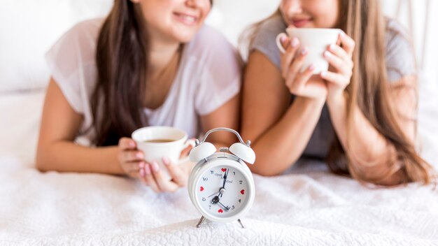 Alarm clock on the bed with two women