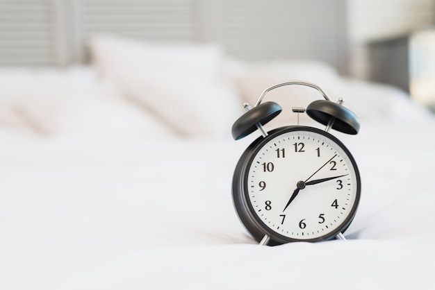 Alarm clock on bed with white linen