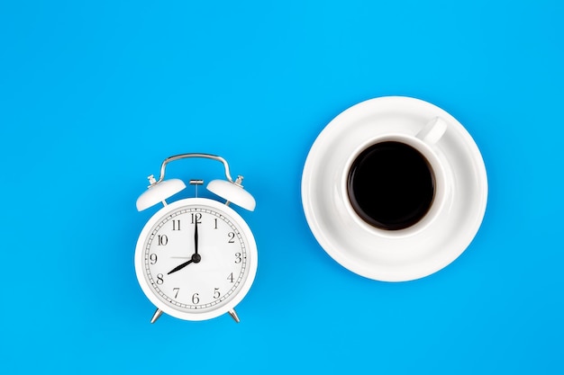 Alarm clock and a cup of coffee on a blue background top view