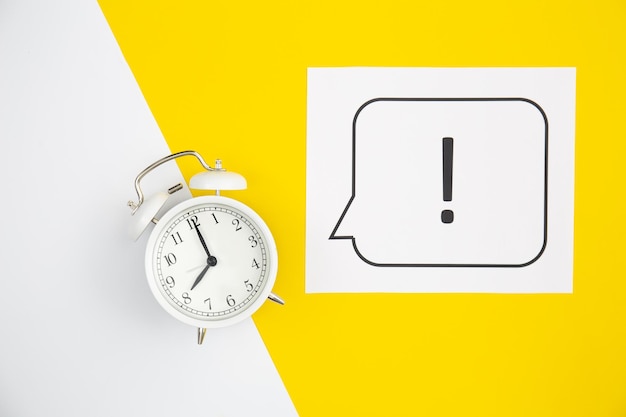 Free photo alarm clock and exclamation mark on yellow background flat lay