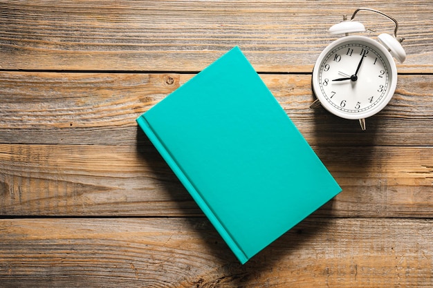 Free photo alarm clock and a green book on a wooden background top view