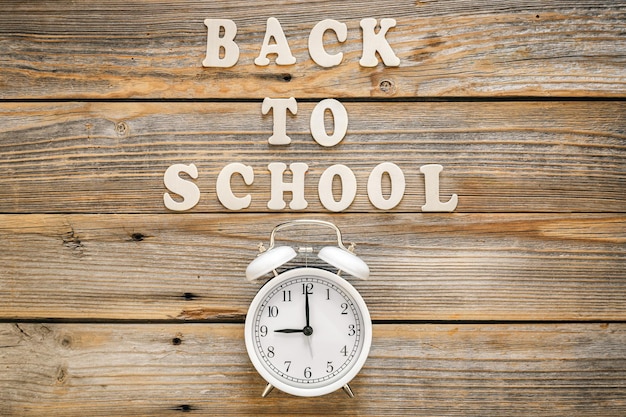 Alarm clock and inscription back to school on a wooden background top view