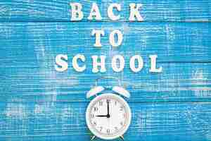 Free photo alarm clock and inscription back to school on a wooden background top view