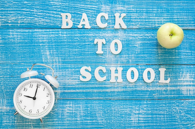 Alarm clock and inscription back to school on a wooden background top view