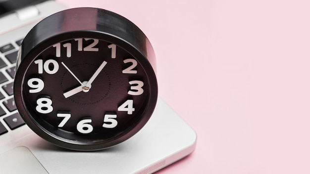 ピンクの背景のラップトップ上の目覚まし時計