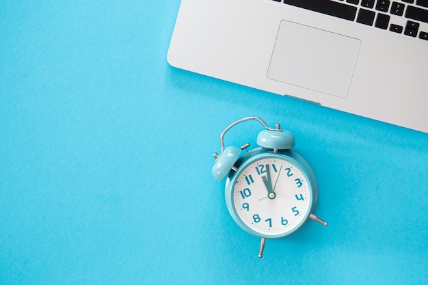 Alarm clock and laptop on a blue background flat lay