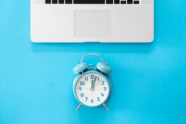 Alarm clock and laptop on a blue background flat lay