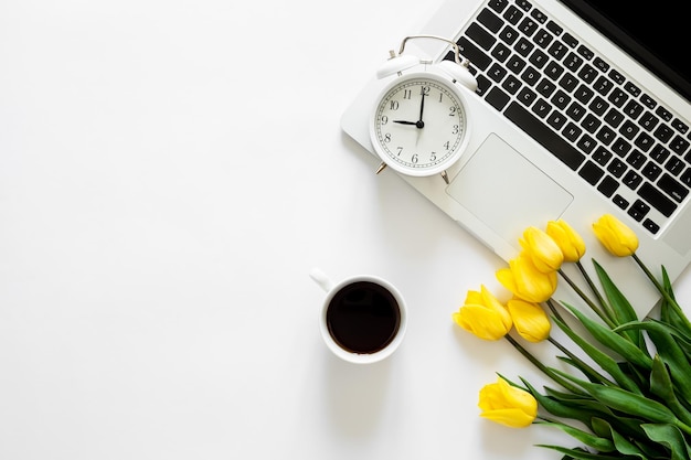 Alarm clock laptop and a bouquet of tulips on a white background top view