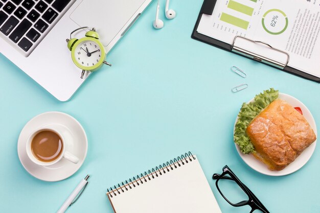 Alarm clock on laptop,earphones,spiral notepad,eyeglasses and budget plan on blue backdrop