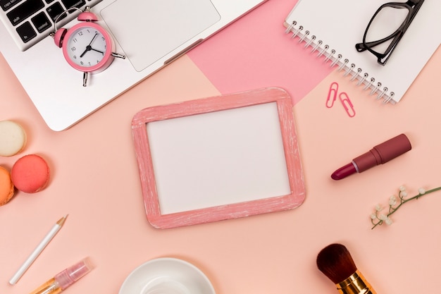 Alarm clock on laptop with makeup brush,macaroons,whiteboard slate on colored background