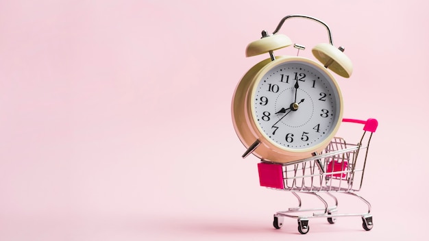 ピンクの背景に対してミニチュアショッピングトロリーの目覚まし時計