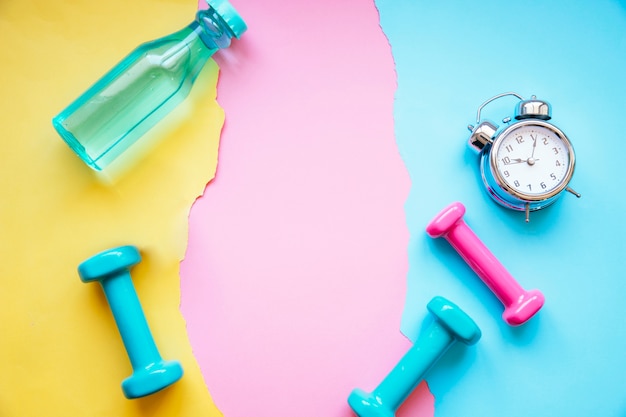 Alarm clock near dumbbells and bottle