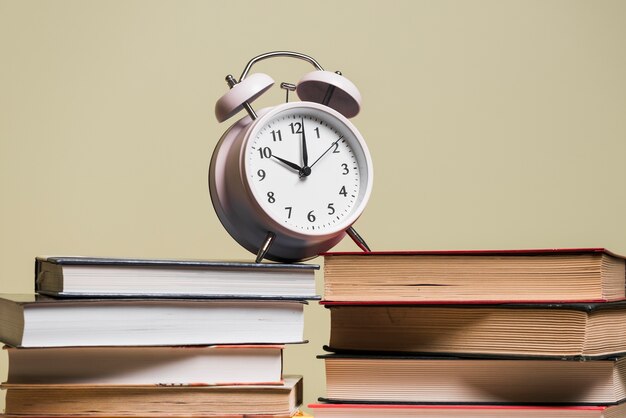Alarm clock on stack of bookshelf against colored background