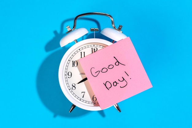 Free photo alarm clock and sticker with the inscription good day on a blue background