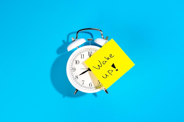 Free photo alarm clock and a sticker with the inscription wake up on a blue background