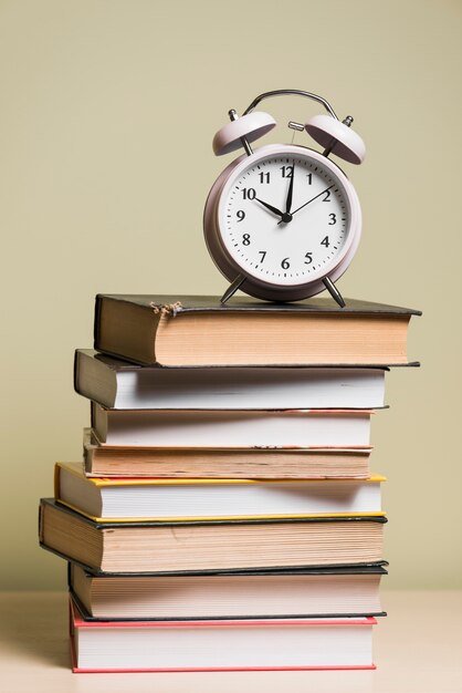 나무 책상 위에 쌓인 책 위에 알람 시계