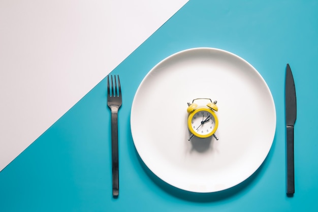 파란색 배경에 나이프와 포크가 있는 흰색 접시에 알람 시계