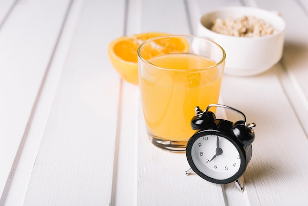 Alarm clock with glass of juice and oatmeal on white table