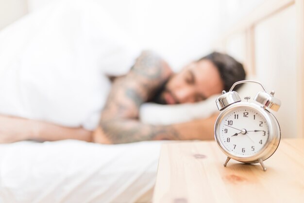 背景で眠っている男と木製の机の目覚し時計