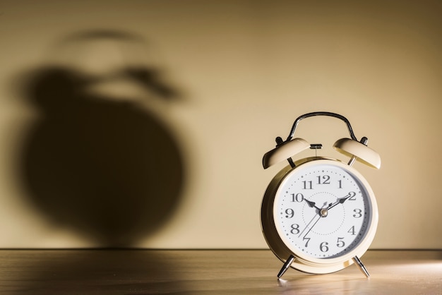 Alarm clock over wooden desk with shadow on wall