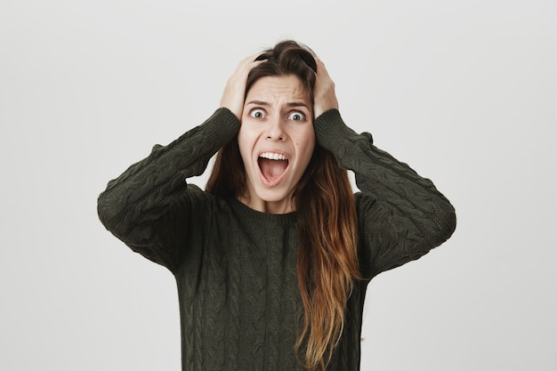 Free photo alarmed scared young woman scream, hold hands on head distressed