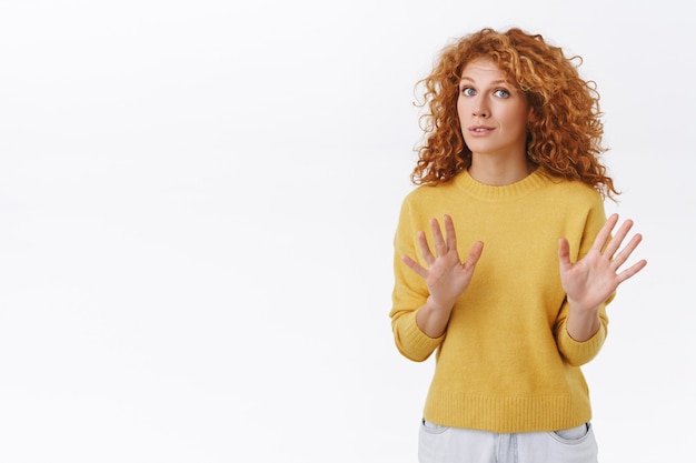 Foto gratuita la donna rossa riccia allarmata e preoccupata calma la persona, dicendo di non sparare, alzando le braccia, implorando di fermarsi, sembrare fuori di testa o nervosa, persuadere qualcuno a far cadere la pistola, muro bianco