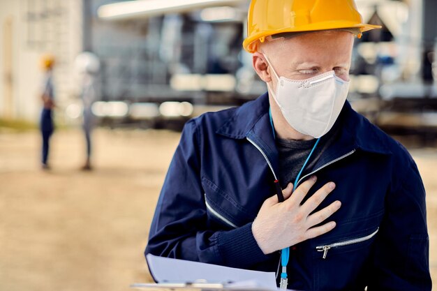 Строитель-альбинос в маске держит грудь от боли во время работы на открытом воздухе