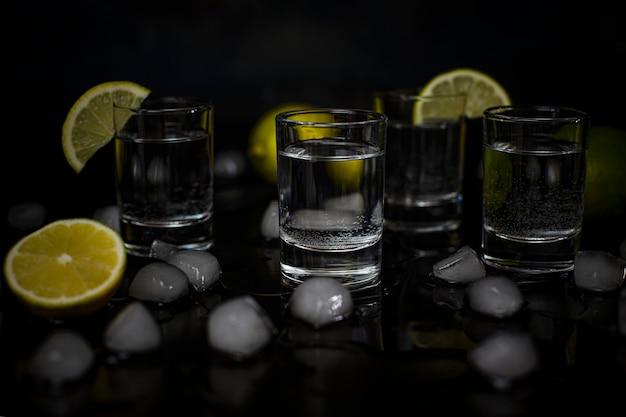 Alcohol shots with lime and ice cubes on black 