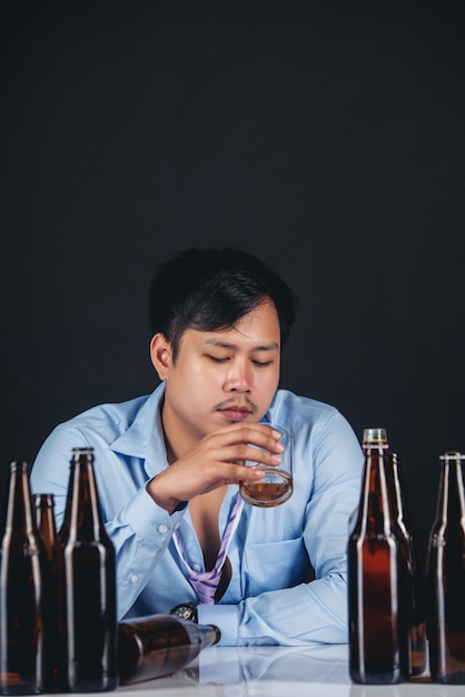 Free photo alcoholic asian man drinking whisky with a lot of bottles