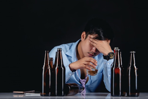 alcoholic asian man drinking whisky with a lot of bottles