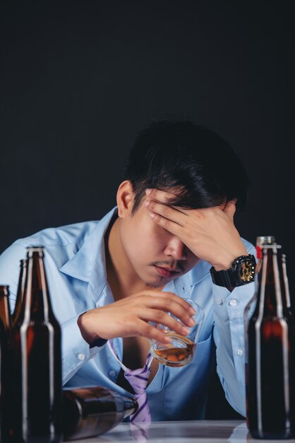 алкоголик азиатский мужчина пьет виски с большим количеством бутылок