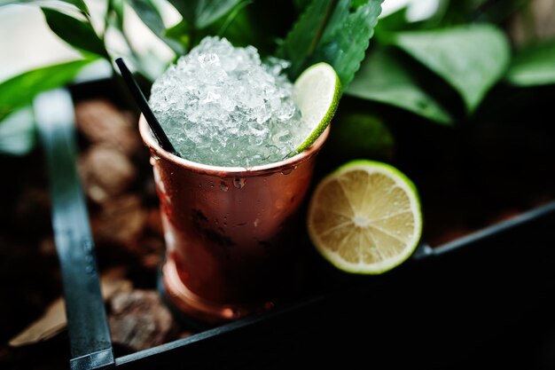 Alcoholic cocktail with ice and lime in bronze can glass on bar table