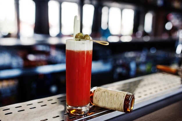 Foto gratuita cocktail alcolico lungo con olive in vetro al tavolo da bar