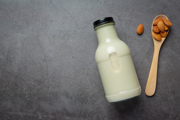 Almond milk in bottle with almond on dark background