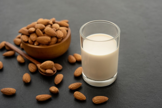 Almond milk with almond in a wooden spoon and bowl on black background.