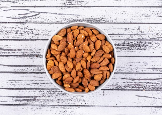 Almond in a white bowl on a white wooden table. top view.