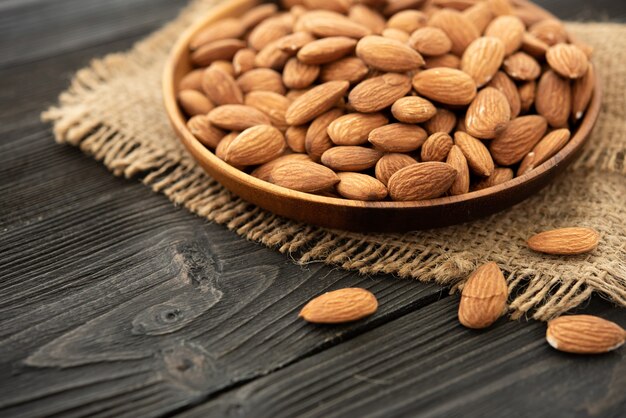 Almond in a wooden bowl. on a wooden background, near a bag from burlap. Healthy food and snack, organic vegetarian food.