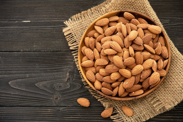 Free photo almond in a wooden bowl. on a wooden background, near a bag from burlap. healthy food and snack, organic vegetarian food.