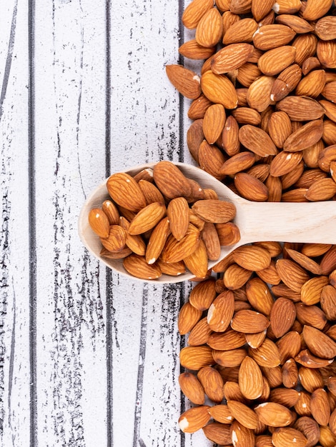 Almond in a wooden spoon on white wooden table. top view.