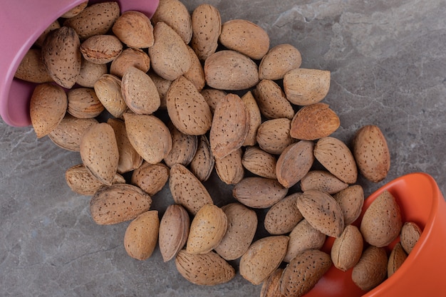 Free photo almonds falling from overturned containers on the marble surface