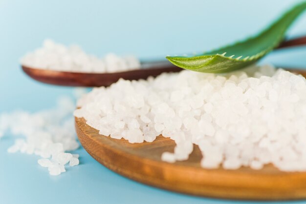 Aloe Vera leaf on rock salt over the wooden tray on blue background