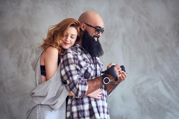 Free photo amateur bearded photographer and a redhead female posing over light grey background.